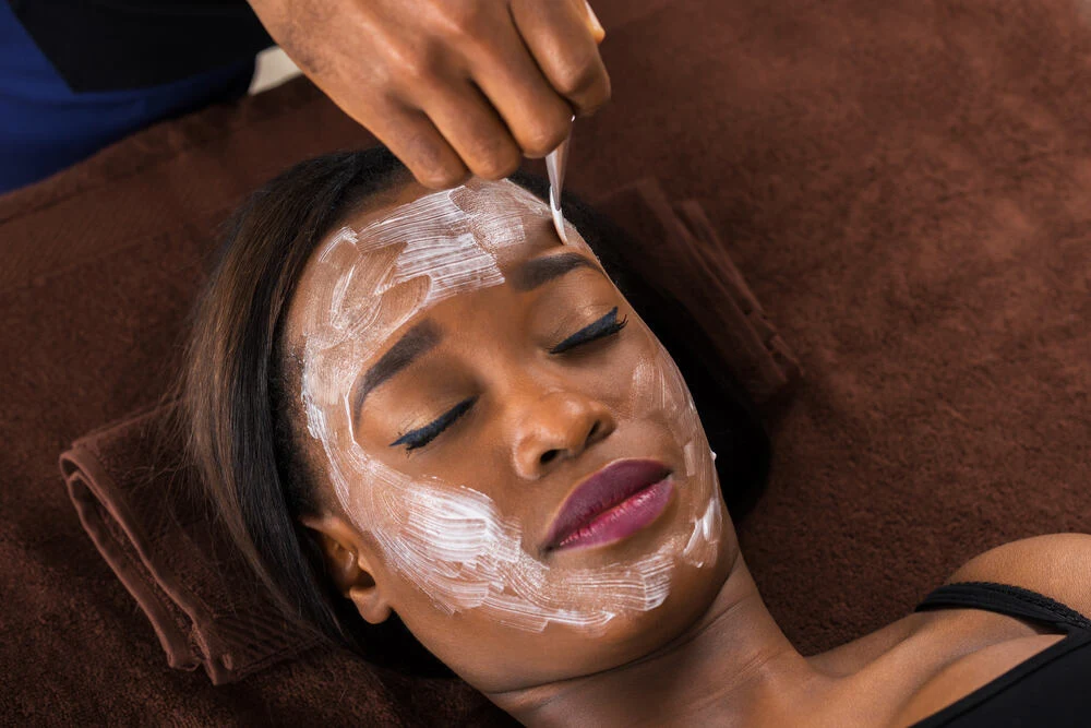 Close-up Of Young African Woman Applying Facial Mask In Spa