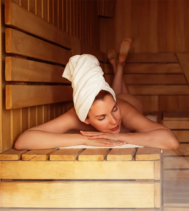 Young woman relaxing and sweating in hot sauna wrapped in towel.