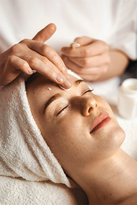 Beautician's hands applying anti-aging facial cream, massaging on woman face.