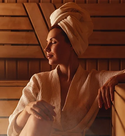 Young woman relaxing and sweating in hot sauna wrapped in towel.